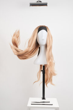 Natural looking blonde wig on white mannequin head. Long hair on the plastic wig holder isolated on white background, front view.