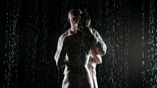 middle-aged man kissing naked young woman standing in rain in darkness, lovers in night, sensuality