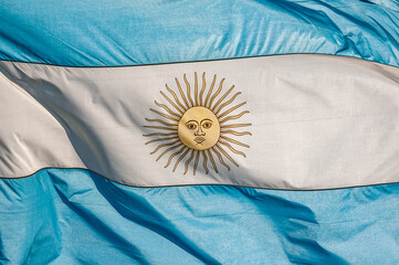 Full frame closeup photo of the Argentine flag, blue and white, with the yellow sun in the center, waving.