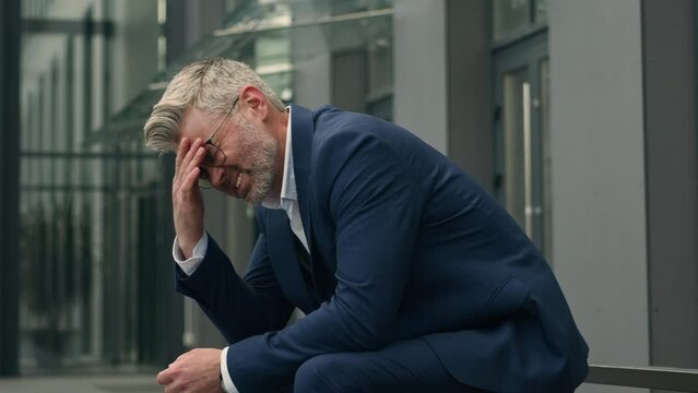 Caucasian old senior businessman feel bad unwell upset mature business man stressed middle-aged stress despair employer in city outdoors feeling headache migraine suffering problem take off glasses