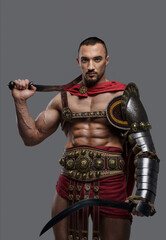 Elegant gladiator in stylish light armor holds two gladii in hands while striking a pose against a gray backdrop