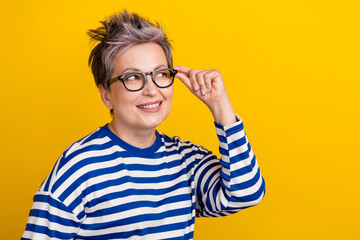 Portrait of minded retired lady wear striped trendy long sleeve shirt touch eyeglasses look thoughtful isolated on yellow color background