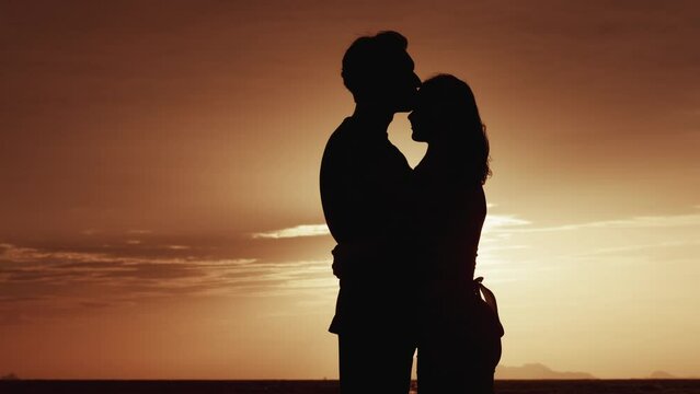 Silhouette of a couple in love at sunset. A man hugs his beloved woman, in the evening at sunset. Male and female stand in an embrace in the evening near the sea. Love concept