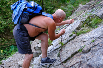climber man with backpack climbs to iron chain on rock, Dangerous path exploration, Wilderness...