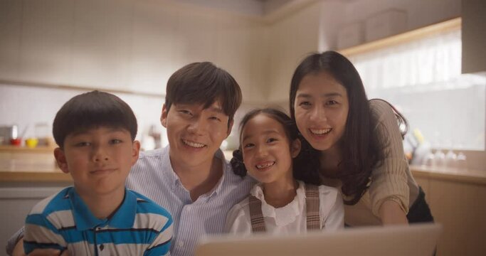 Portrait of Happy Korean Family Using Laptop Computer then Looking at the Camera and Smiling. Young Parents and Two Adorable Kids Watching Photos and Memories from their Last Trip Together