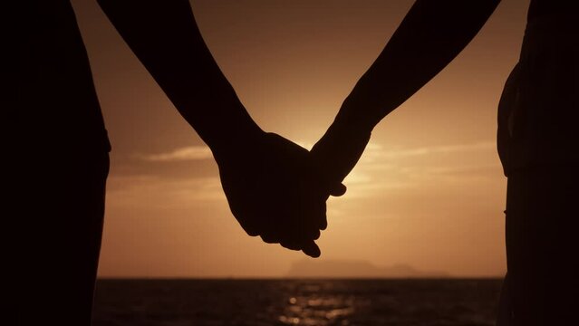 Close-up silhouette of man extending his hand and a woman takes his hand. Concept of mutual understanding, love and support. Romantic couple take each other's hands during a date on sunset or dawn