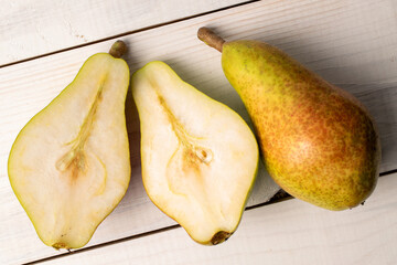 One whole and two halves of organic juicy pears, close-up, on a white wooden table, top view.