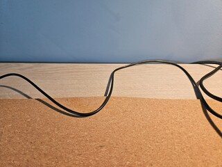Looking down from a high angle view at a black electrical cord curling over the surface of a beige colored office desk against a blue wall.
