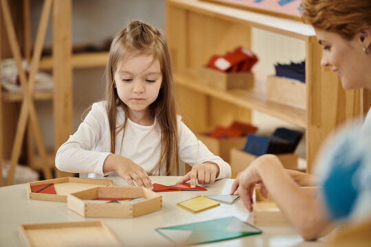 smiling teacher playing with girl and didactic material on table in montessori school