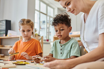 Obraz na płótnie Canvas interracial children playing with didactic montessori material near female teacher, diversity