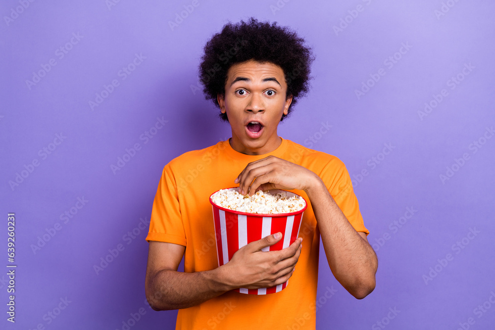 Wall mural Photo of shocked funny youth man open mouth emotions astonished hold bucket popcorn intrigue dc film isolated on violet color background