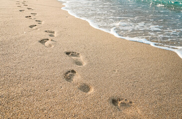 Footprints of human feet on the sand near the water on the beach - Powered by Adobe
