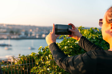 Girl taking photo other phone of Plymouth harbour at sunset