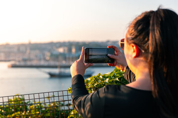 Girl taking photo other phone of Plymouth harbour at sunset