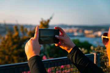 Girl taking photo other phone of Plymouth harbour at sunset