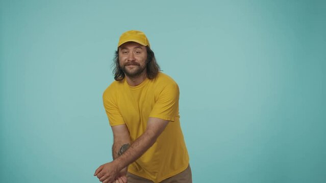 Delivery man in yellow uniform tries to cath a box with fragile stickers but misses it, looks shocked and clueless. Isolated on blue background.
