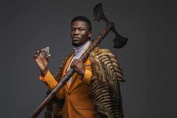 Dark-skinned man in a stylish yellow jacket, draped in the pelt of a wild animal holds massive...