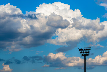 Blue sky with white and dark cloud.  Tall Stadium Lights Towering in the Air.
