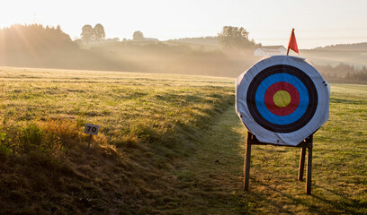 Archery target at an archery course with golden sunrise and fog in the background