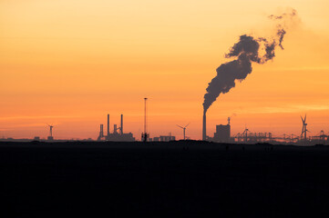 Power station with sunset as a silhouette. With steam in the sky. Nature with industry.