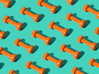 Creative pattern composition made of orange dumbbells on pastel green background. Minimal fitness,...