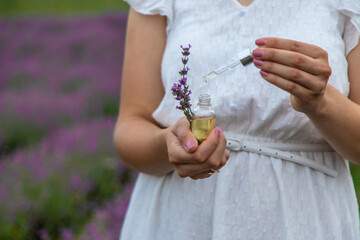 Woman holding bottle with natural essential oil in lavender field. Selective focus