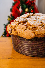Panettone natalizio classico artigianale fotografato su un tavolo di legno con sullo sfondo un albero di natale