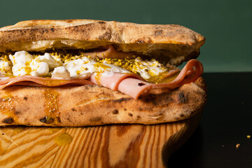 Panuozzo napoletano ripieno di mortadella, burrata pugliese, pesto di pistacchio e granella di pistacchio poggiato su un tagliere di legno © Vincenzo VAD