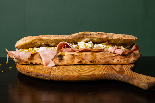 Panuozzo napoletano ripieno di mortadella, burrata pugliese, pesto di pistacchio e granella di pistacchio poggiato su un tagliere di legno