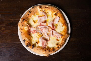 Pizza gourmet napoletana con mozzarella, pancetta e formaggio fotografata dall'alto su un tavolo di legno 