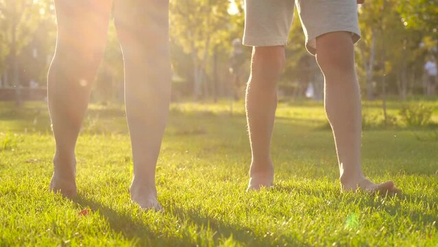 mom and child walk on the green grass in the park. Close-up of bare female children feet. A happy boy walks with his mother through the meadow. kids dreams,