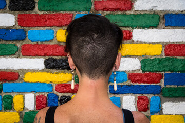 Una donna di spalle con i capelli corti guarda un muro  di mattoncini colorati