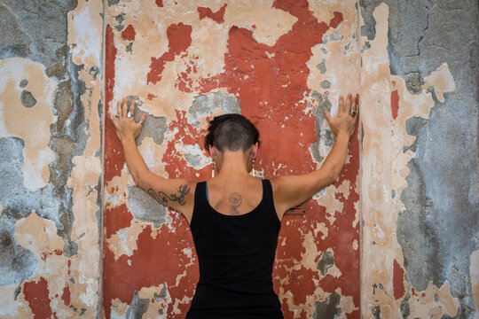 Una donna infelice si appoggia ad un muro rosso e azzurro dall&rsquo;intonaco scrostato a Burano, isola della laguna di Venezia
