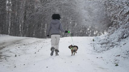 Young woman running with french bulldog dog in the mountain forest winter snow landscape, slow motion