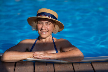 An elderly woman in a boater hat swims in the pool. Vacation in retirement. 