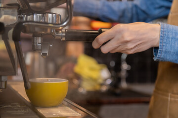 Close-up anonymous barista hands using professional coffee machine making hot espresso and pouring coffee to mug in cozy cafe, small businesses start up for young people lifestyle concept