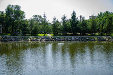 A pond surrounded by a monument and green trees with a lawn © Alexander