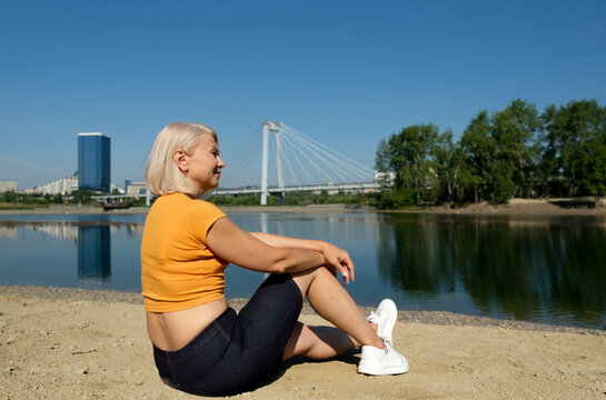 Back view of Senior woman looking lake on a beach. Concept of healthy active life outdoor. Female near the public pond in a city.