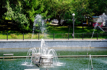 A pond with working fountains, surrounded by a monument of trees and lawn