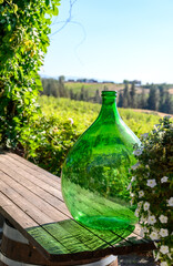 A large glass green bottle of wine stands on a wooden table against the backdrop of a magnificent landscape. Focus on the bottle.Vertical photo