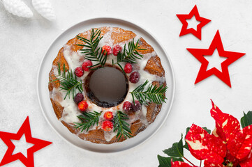Christmas bundt cake with white icing, rosemary branches and cranberries on a white background with...