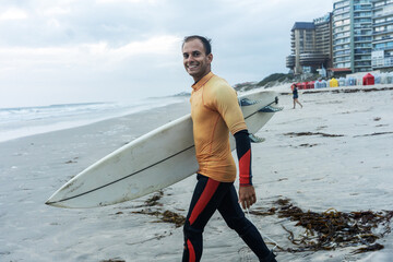 Portrait of male surfer s walking  toward the water. Board in hand, wetsuit on, ready for an...