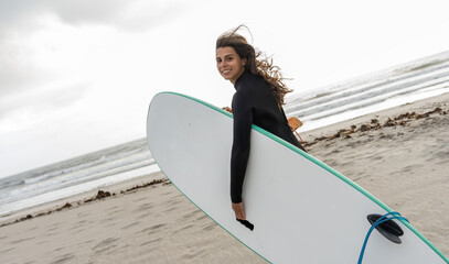 Portrait of female surfer s walking  toward the water. Board in hand, wetsuit on, ready for an...