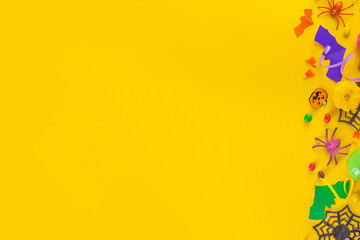 Halloween high-colored yellow background with colorful party holiday accessories and decor, spiders, cobwebs, pumpkins, bats, ghosts, top view flat lay copy space