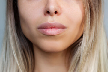 Cropped shot of young caucasian blonde woman's face with perfect lips after lip enhancement. Injection of filler in lips on a gray background. The result of lip augmentation. Close up