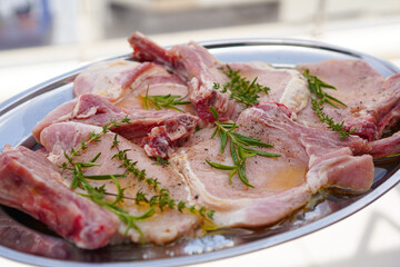Closeup of Fresh raw pork chops bone steak with rosemary, thyme and olive oil on a silver tray