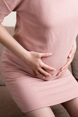 Pregnant Lady Having Massaging Lower belly Sitting On Sofa Indoor. Pregnancy Problems Concept. Maternity healthcare