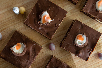 Square slices of chocolate cake with chocolate eggs of various sizes lie on a wooden table near a...