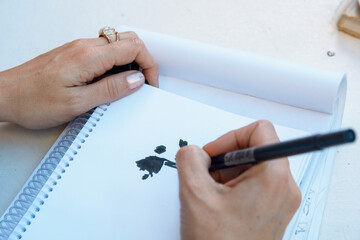 female caucasian hands of unrecognizable woman drawing on white paper with black colored marker indoors