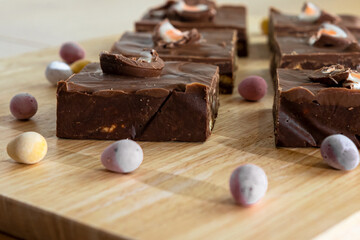 Slices of chocolate cake with chocolate eggs of various sizes are placed on a wooden table near a chef